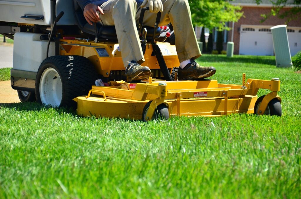 person operating a yellow Hustler Turf zero-turn mower to maintain a manicured lawn.